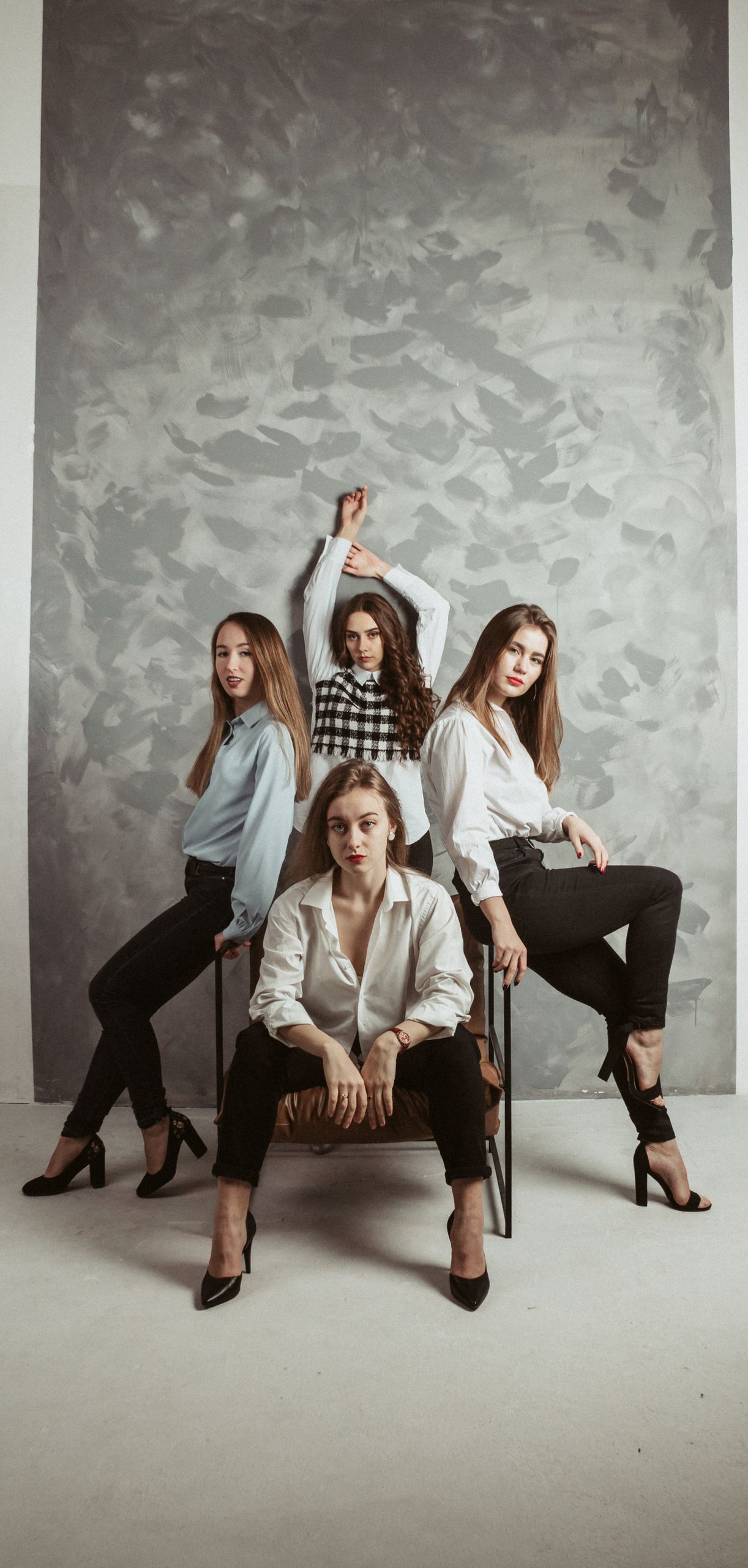 Elegant studio portrait of four stylish women posing confidently against a textured backdrop.