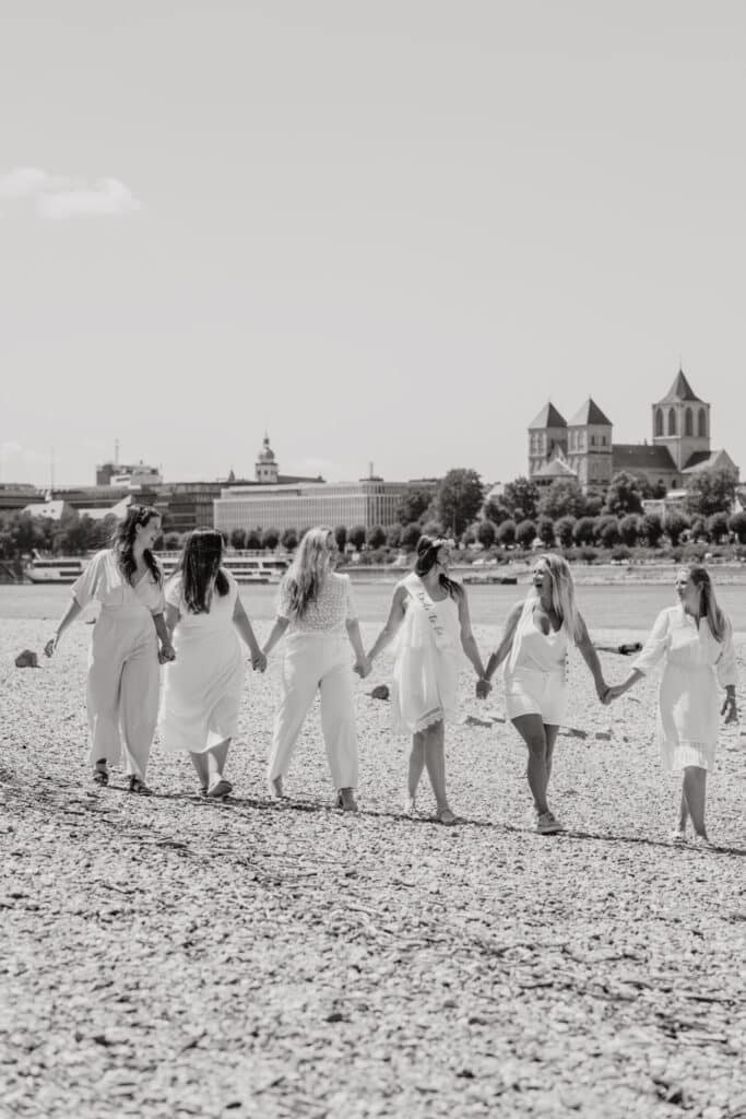 Schwarz-weiß einer Freundesgruppe aus 6 Personen, die alle Hand in Hand an einem Sandufer gehen. - Fotospots Köln